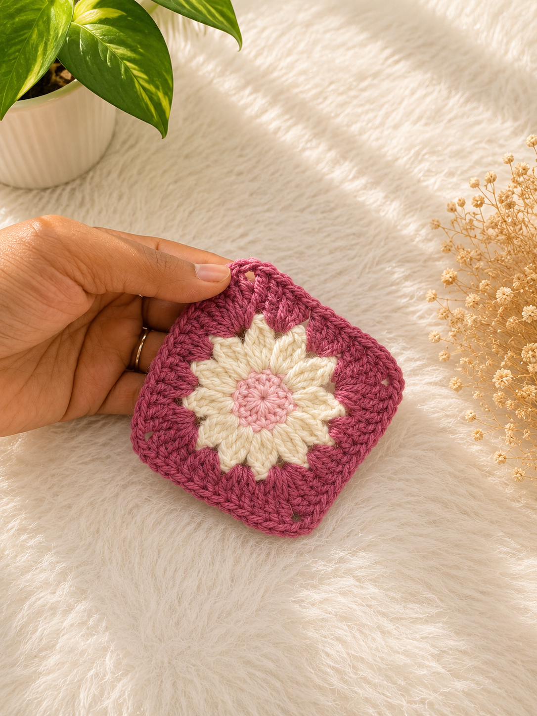 Handmade daisy-inspired crochet coaster featuring pink and ivory floral detailing crafted from premium cotton yarn by The Hook Project.