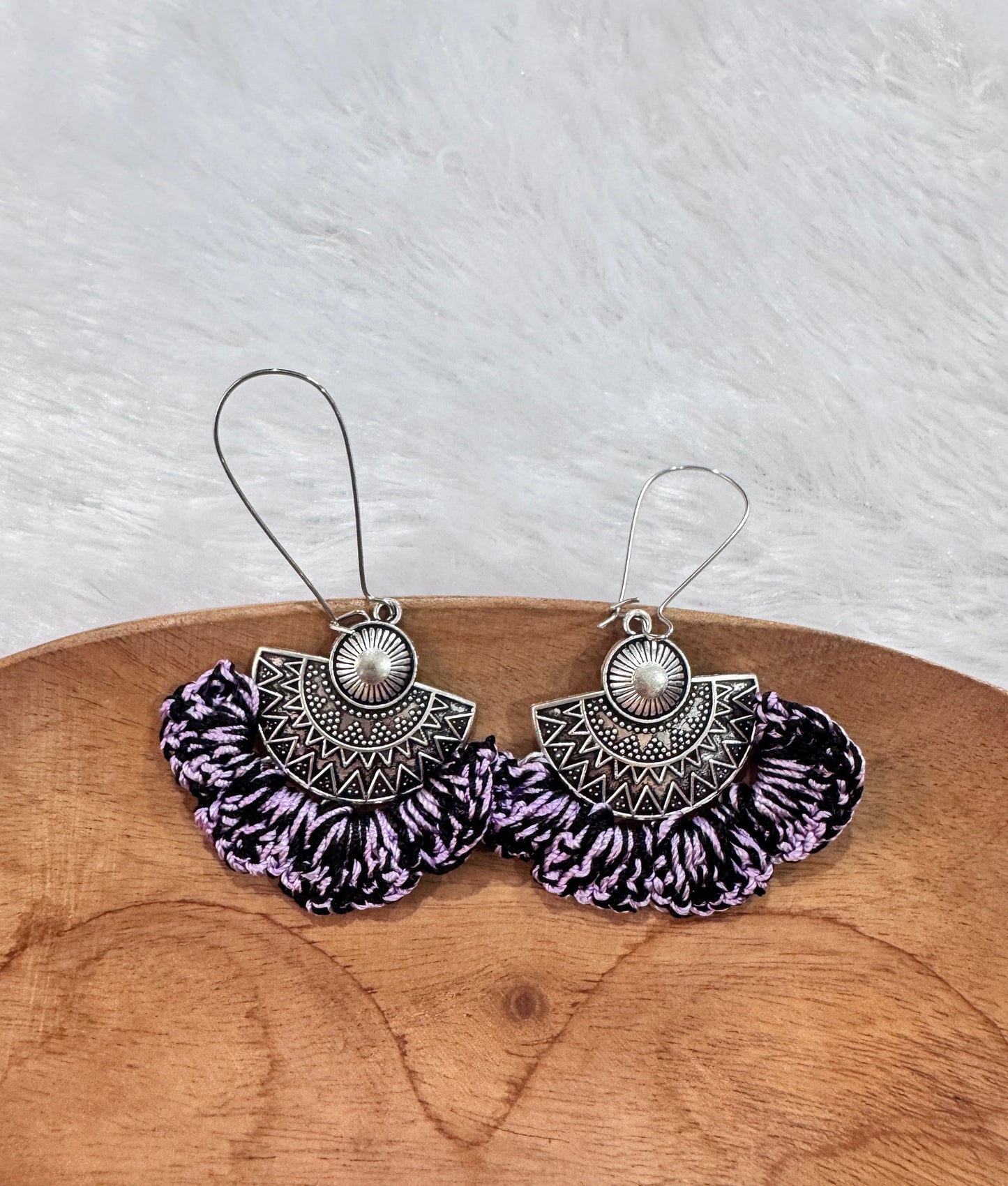 Handmade lavender and black crochet earrings with oxidized silver-tone metal detailing displayed on a wooden tray
