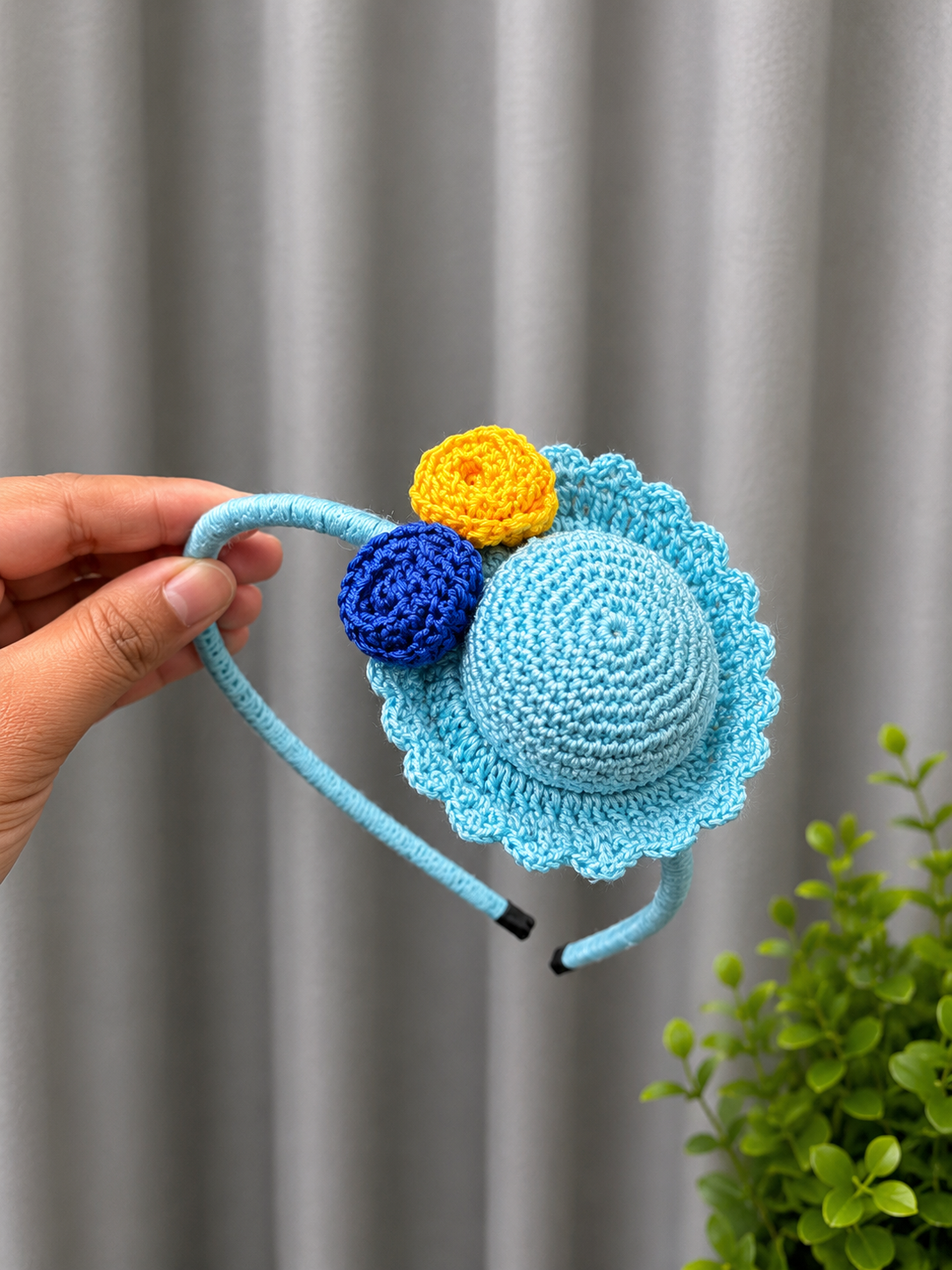 Handmade sky blue crochet hat-style headband with yellow and royal blue floral accents on a fabric-covered headband.