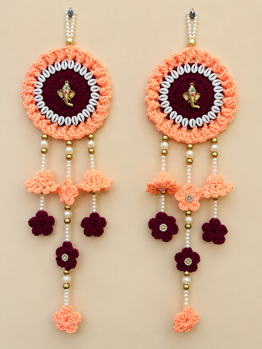 Ganeshika crochet wall hanging set of 2 in coral-peach and burgundy with golden Ganesha embellishments, white decorative accents, pearl-style beads and floral tassels.