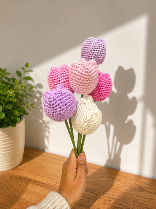 Set of 6 multicoloured handmade crochet tulips in pastel pink, lavender, ivory and bright pink shades, arranged as a bouquet with green stems.