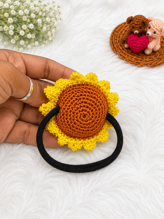 Handmade sunflower crochet hair tie with yellow petals and brown center attached to a black elastic hair band.