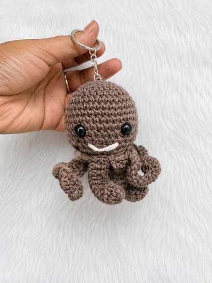 Handmade crochet octopus keychain available in multiple colors and sizes, featuring a smiling amigurumi octopus with curled tentacles and metal keyring by The Hook Project.