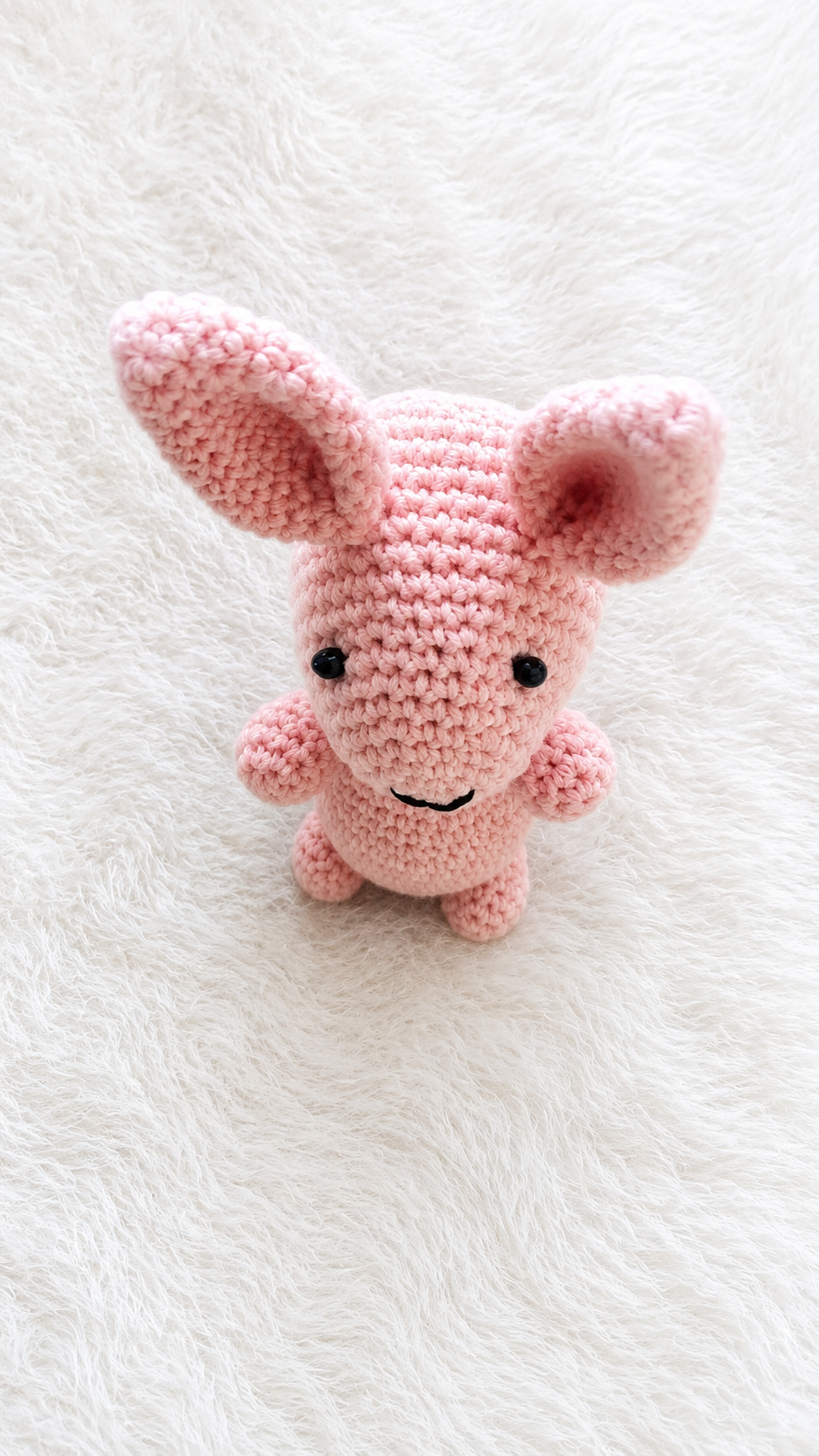 Handmade pink crochet bunny plush toy with long ears lying on a soft white furry background.