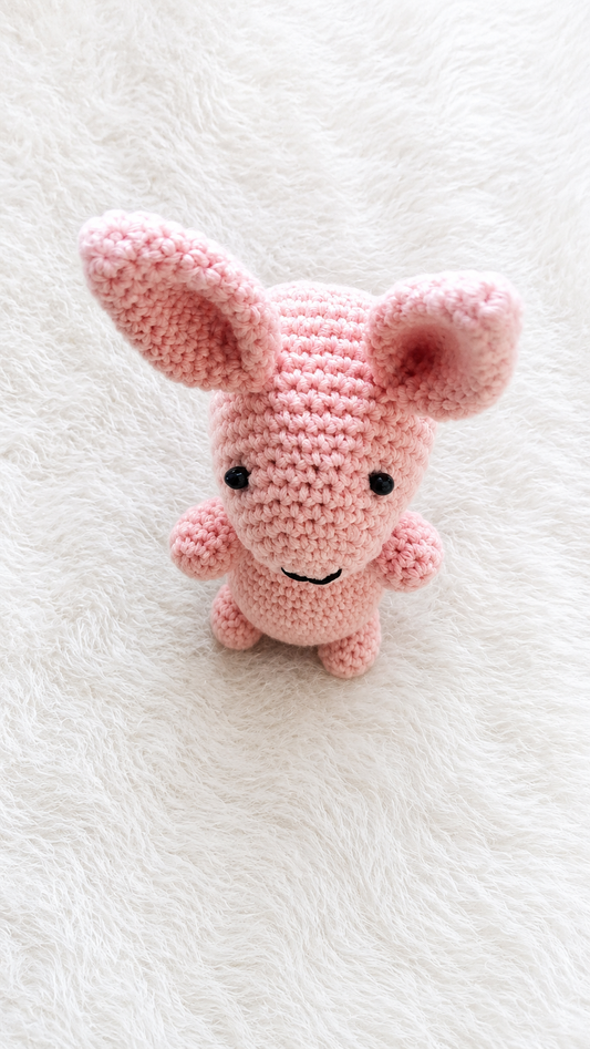 Handmade pink crochet bunny plush toy with long ears lying on a soft white furry background.