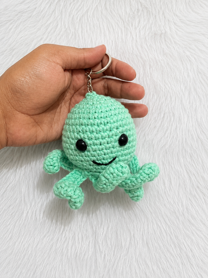 Handmade crochet octopus keychain available in multiple colors and sizes, featuring a smiling amigurumi octopus with curled tentacles and metal keyring by The Hook Project.