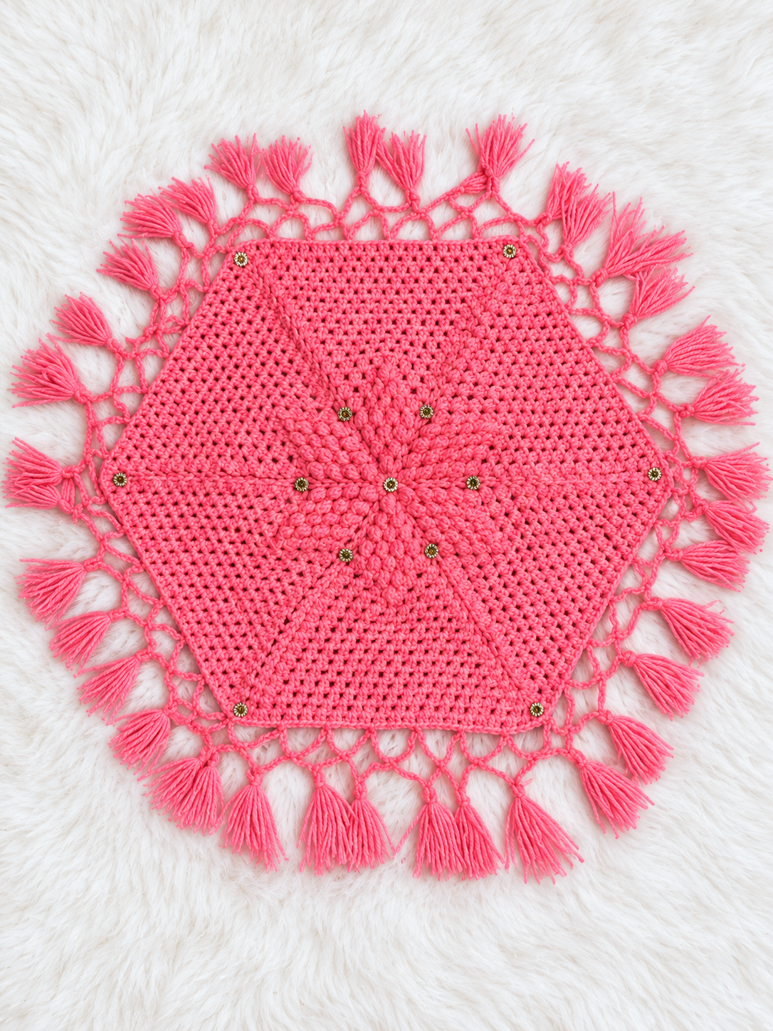 Coralia coral pink crochet thaal paros with a hexagonal centre, openwork border, matching long tassels and gold-tone embellishments for festive pooja décor.