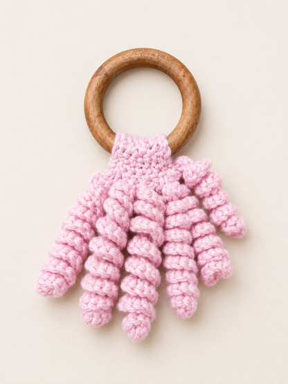 Handmade pink crochet baby teether with natural wooden ring and soft curly cotton texture for teething relief.