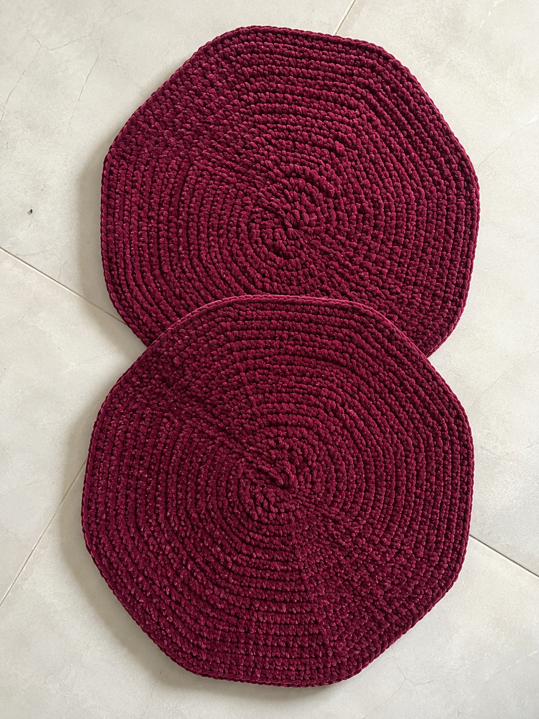 Set of two handcrafted burgundy crochet table mats made from soft velvet chenille yarn displayed on a light background with decorative greenery