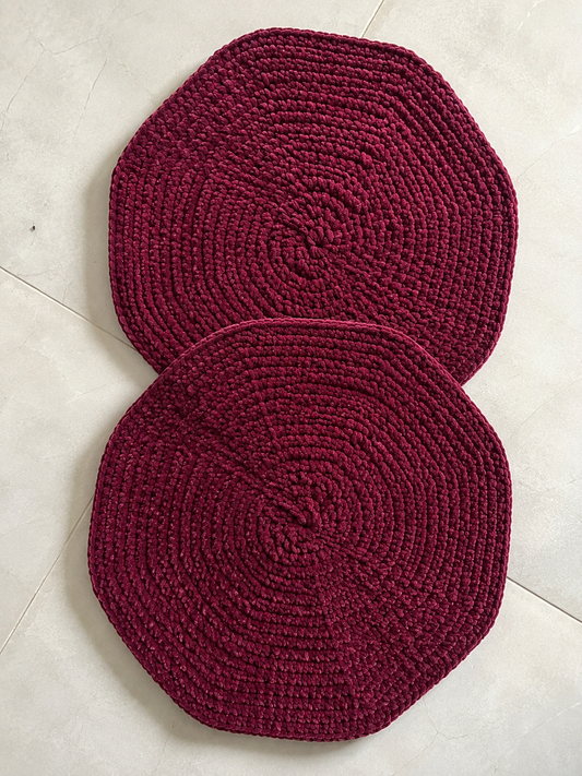 Set of two handcrafted burgundy crochet table mats made from soft velvet chenille yarn displayed on a light background with decorative greenery