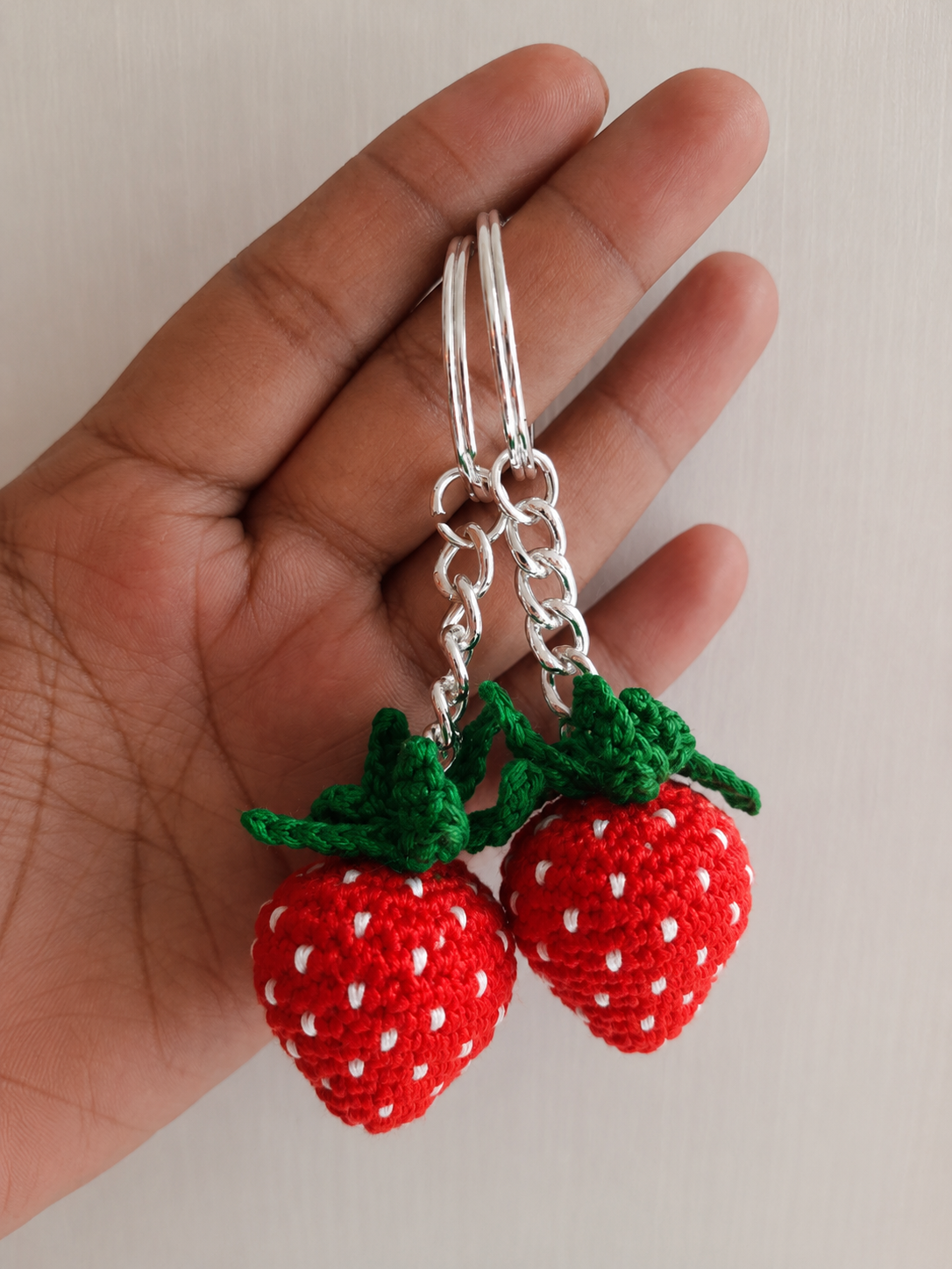 Handcrafted crochet strawberry keychain with embroidered white seeds and green leaves attached to a metal keyring by The Hook Project