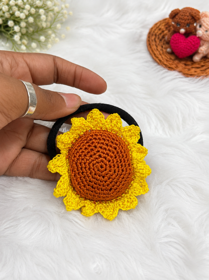 Handmade sunflower crochet hair tie with yellow petals and brown center attached to a black elastic hair band.