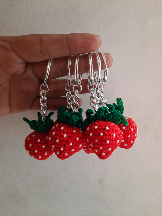 Handcrafted crochet strawberry keychain with embroidered white seeds and green leaves attached to a metal keyring by The Hook Project