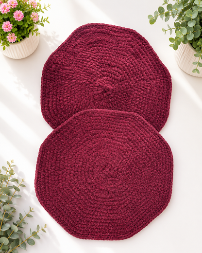 Set of two handcrafted burgundy crochet table mats made from soft velvet chenille yarn displayed on a light background with decorative greenery