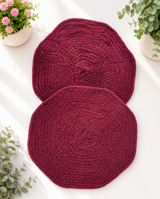 Set of two handcrafted burgundy crochet table mats made from soft velvet chenille yarn displayed on a light background with decorative greenery