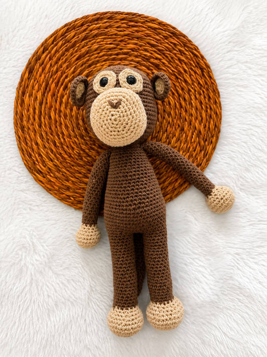 Crocheted monkey toy on a textured brown circle with a white background