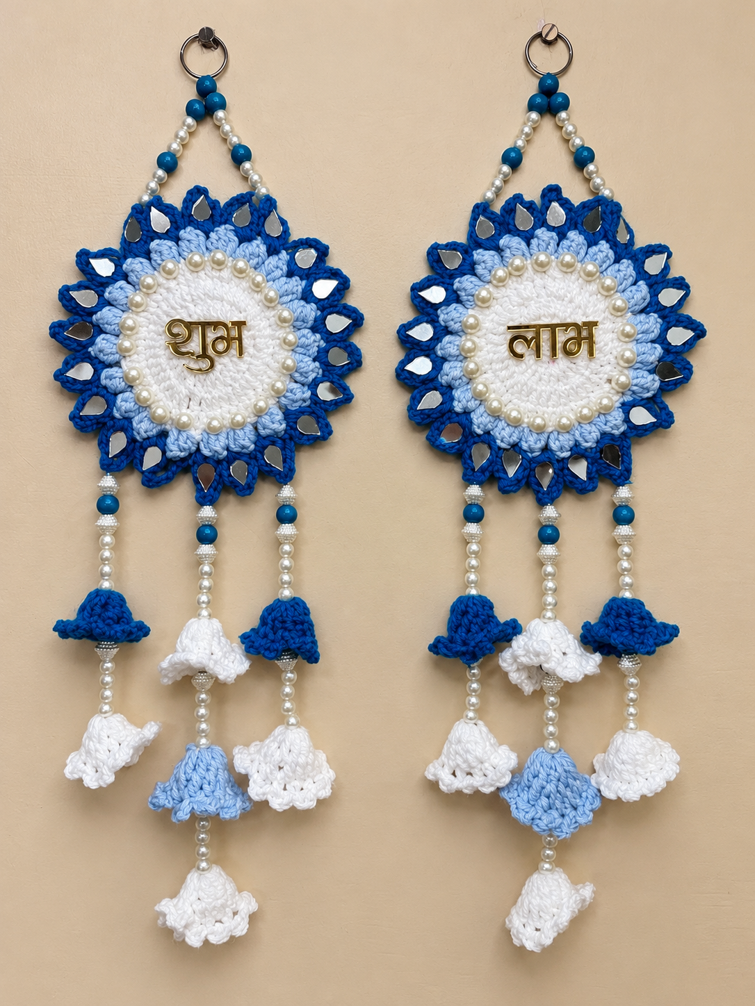 Shubh Labh crochet wall hanging set of 2 in white, light blue and royal blue with Hindi lettering, pearl-like detailing, reflective accents and crochet bell tassels.