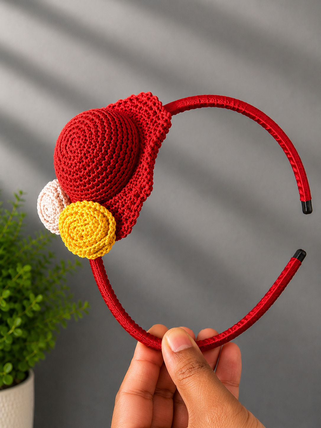 Handmade ruby red crochet hat headband with yellow and ivory floral accents on a satin-wrapped headband, displayed against a neutral background.