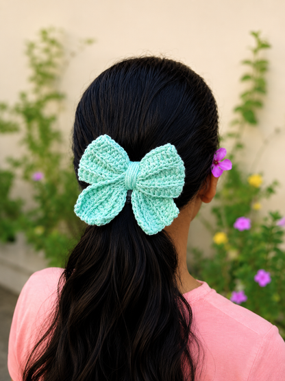 Handmade mint green crochet bow hair clip styled on a ponytail with a garden-inspired background.
