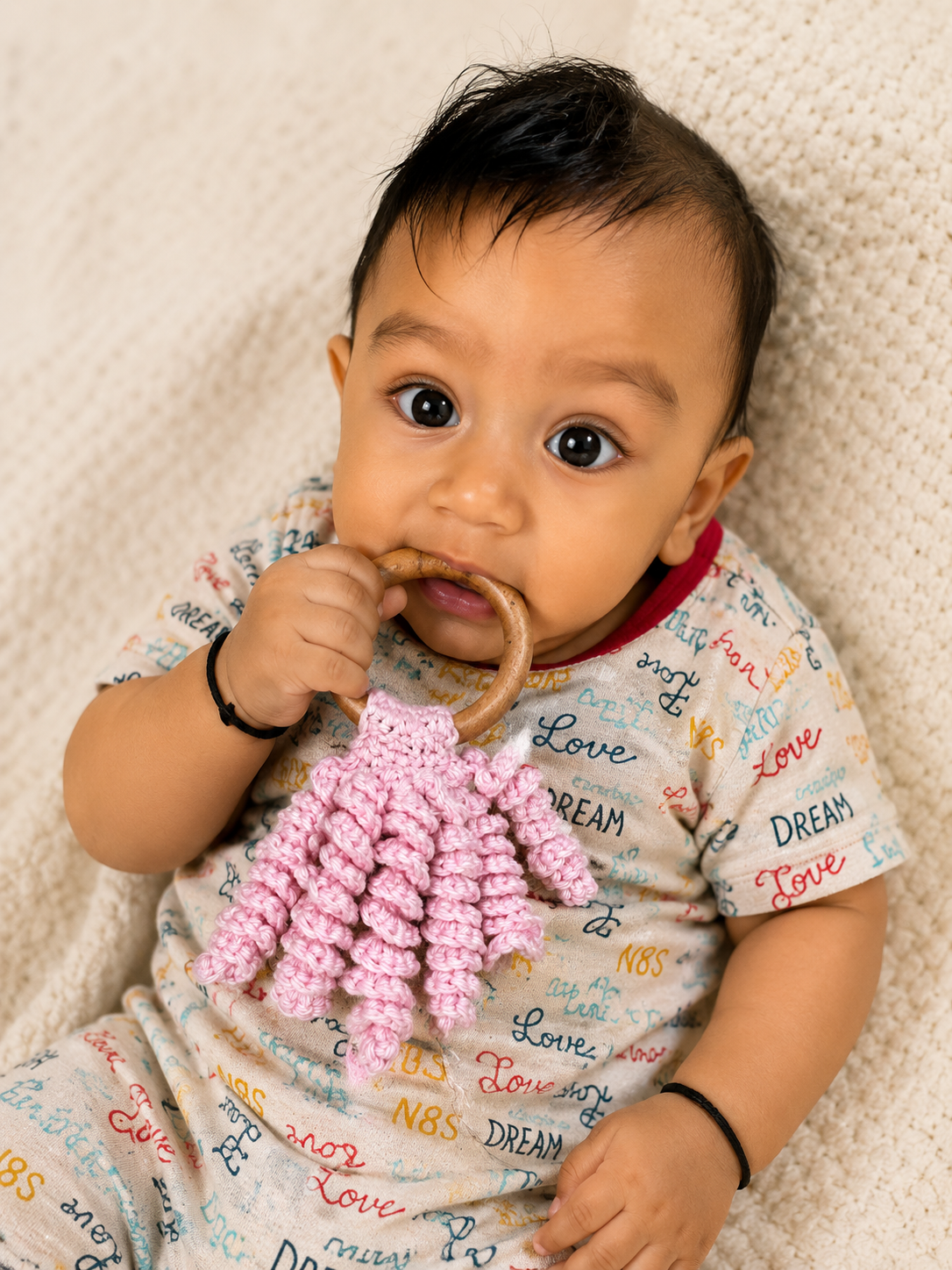 Handmade pink crochet baby teether with natural wooden ring and soft curly cotton texture for teething relief.