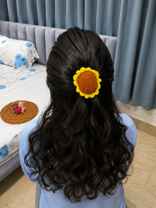 Handmade sunflower crochet hair tie with yellow petals and brown center attached to a black elastic hair band.