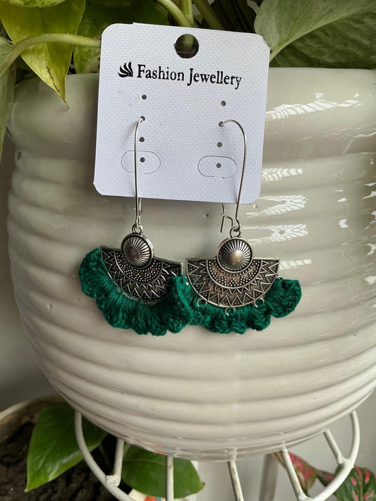 Handmade emerald green crochet statement earrings with silver-tone bohemian charms displayed on a jewellery card.
