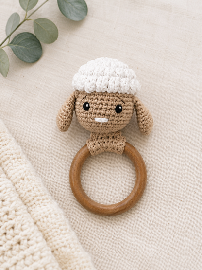 Handmade crochet lamb wooden teether rattle with soft beige and white crochet detailing on a neutral fabric background.