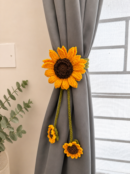 Handmade crochet sunflower curtain tieback with dangling floral accents attached to a grey curtain.