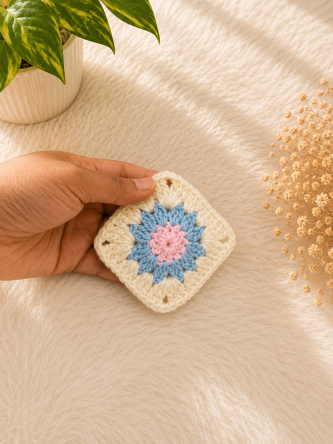 Handmade floral crochet coaster featuring pastel blue and blush pink flower detailing on an ivory granny square base, crafted from premium cotton yarn by The Hook Project.