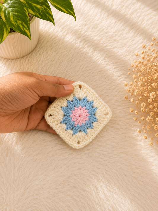 Handmade floral crochet coaster featuring pastel blue and blush pink flower detailing on an ivory granny square base, crafted from premium cotton yarn by The Hook Project.
